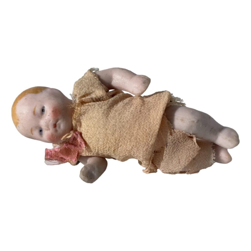Photo of miniature German bisque doll laid on its side with head on left and feet to right. The doll is facing forward.