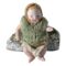 Main photo of German miniature bisque doll displayed leaning against a small rock and forward facing. This little doll is wearing a lacy cap and has pale orange hair painted underneath. It has more of a glossy face with round orange cheeks and small dark orange mouth. The woolly vest appears to be a later addition. Underneath the vest, it is wearing a top similar in design and material to the cap and it wears a pair of knitted short pants. Its left arm is made bent at the elbow.