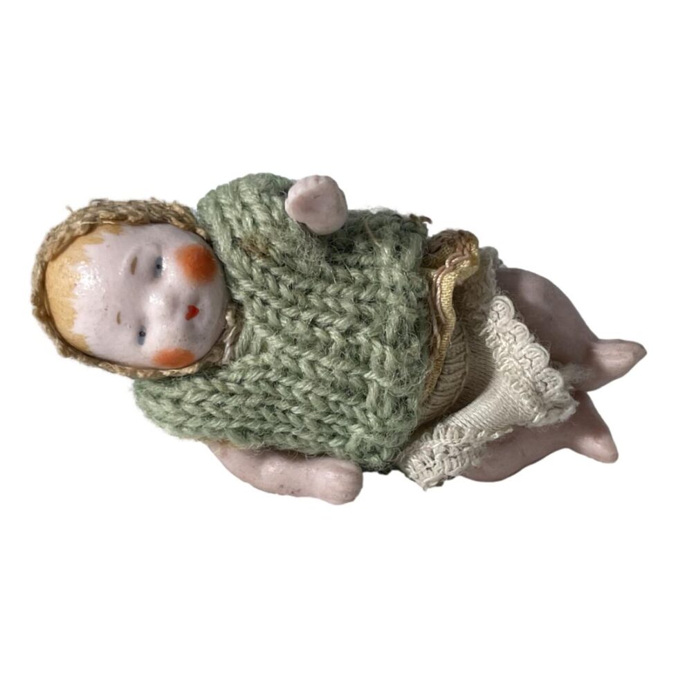 Photo of the bisque miniature doll on its side and forward facing with head on the left.