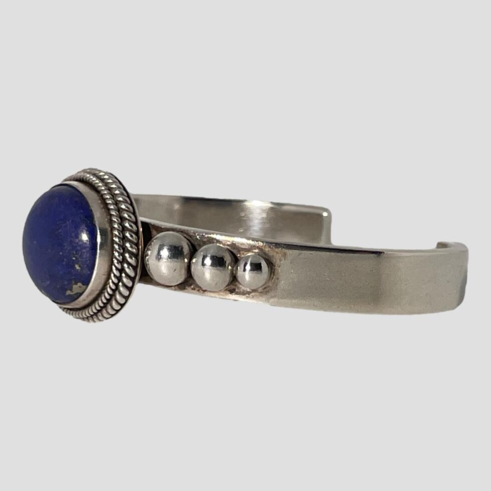 Photo of lapis cuff bracelet on a flat surface with the bracelet front facing left showing one full side of the cuff.
