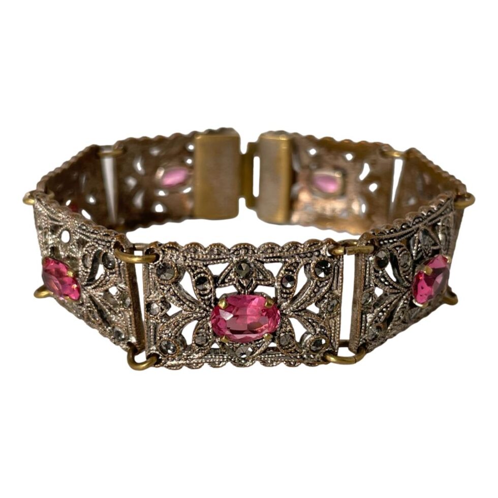 Photo of bracelet displayed in a circle on a flat surface with the clasp closed. The clasp side is visible in the background with a coppery colour on the back of panels (which is a little worn)