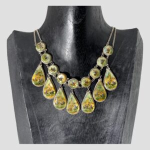 Main photo of Persian hand-painted necklace displayed on a black wooden display stand with the necklace front forward facing. The necklace consists of 9 round panels along the top with 7 teardrop shaped panels hanging below each a piece of mother of pearl. Each hand-painted scene is different showing a sequence of hunting images not dissimilar to old school cartoon making. The colours are primarily yellow and pale green with snippets of blue, white and red on the men and brown and black of the horses. The round panels have a short chain link separating with the double chain extending as the necklace chain. The teardrop panels are attached by a single ring clasp. Each panel image is incredibly detailed and beautiful.