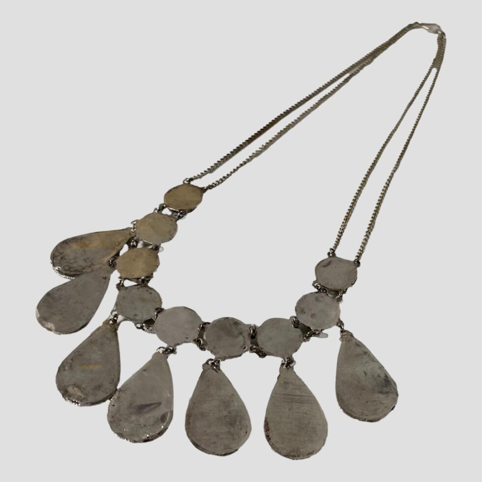Photo of necklace displayed on a flat surface and laid diagonally across the page with the panels in the bottom left. The back of the panels is covered in a thin sheet of silver.