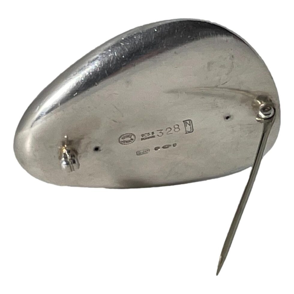 Photo of the back of Jensen oyster brooch showing the hallmarks and the designers initials. The brooch is being propped up by its own pin.