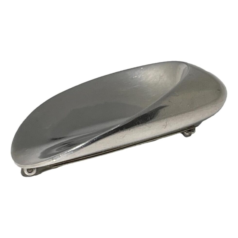 A photo of the Jensen oyster brooch seen from a side angle to show the depth. The smaller end which is deepest is on the right and the wider flatter end on the left.