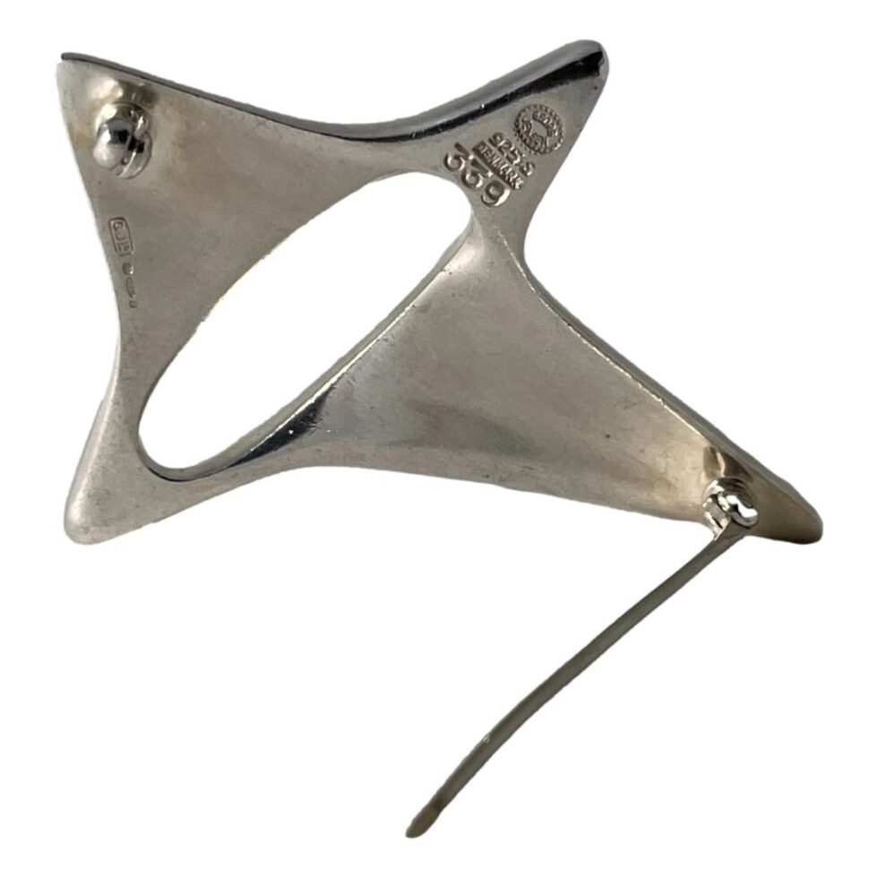 Photo of the back of the Georg Jensen star brooch shown from the back propped up by its pin. The hallmark is visible to the top point as well as below the clasp.