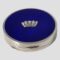 Main photo of blue guilloche enamel compact seen from a slightly raised angle looking diagonally downward to show the whole blue enamel top. The front opening side of the compact is in the foreground with the short hallmark to the left of the opener. The silver naval crown at the centre of the blue guilloche appears as if floating in the blue sea.