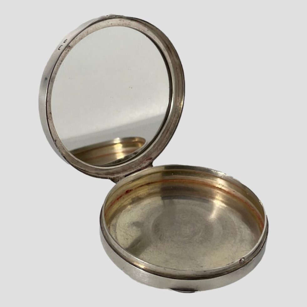 Photo of blue guilloche enamel compact displayed open with the opening side facing towards the bottom right corner. The mirror inside the lid is in very good condition and is reflecting part of the bottom part of compact.