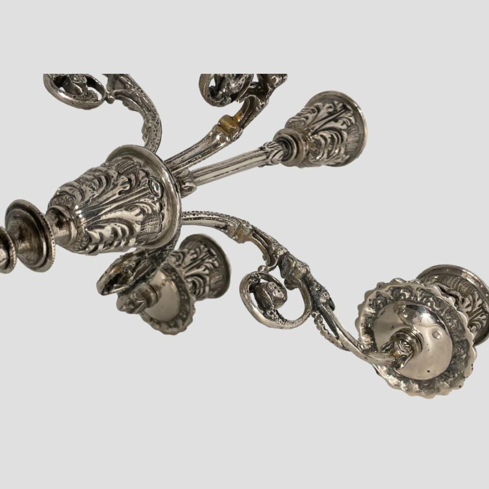 A close up of some of the sconces and arms from the underside with single hallmark visible below the wax drip plate on the lower right.