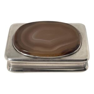 Main photo of antique silver table snuffbox seen from a raised angle looking diagonally down to the agate on the lid with parts of the surrounding silver visible all around. The box is very tactile with a smooth base and lid with rounded corners. The agate is set a little raised at the top with a silver frame surrounding it. The agate is a lovely natural colour bands in cream, pale browns and orange. The middle section of the box in slimmer than the lid and base giving a good grip to open the box lid.