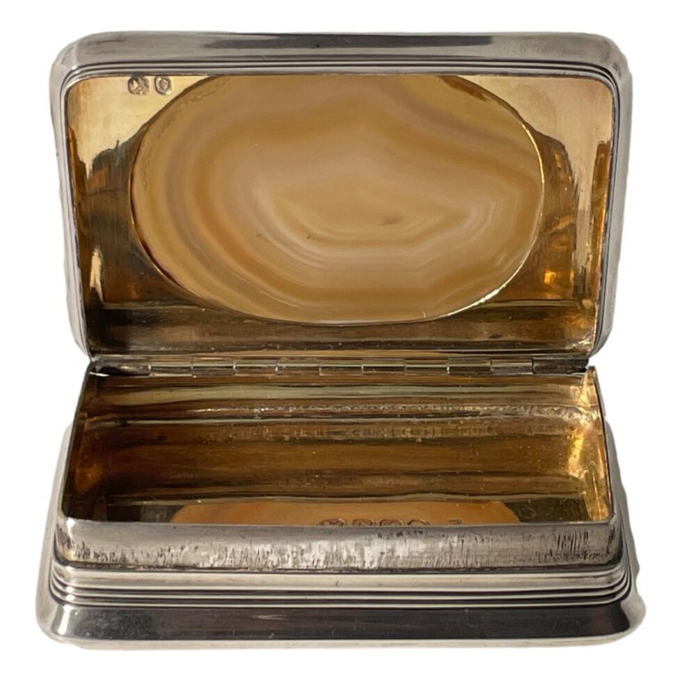 Photo of antique silver table snuffbox displayed from the front with the lid shown open. The lovely lines of the agate in the lid can be seen with the colours of it complimenting the gilt interior of the box. The short hallmark to the top left corner can been seen.