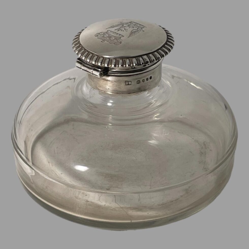 Photo of antique silver mounted inkwell seen with the hinged area at back facing towards the bottom left corner. The full hallmark is visible to the right of the hinge and a fraction of the shorter hallmark is visible above it.