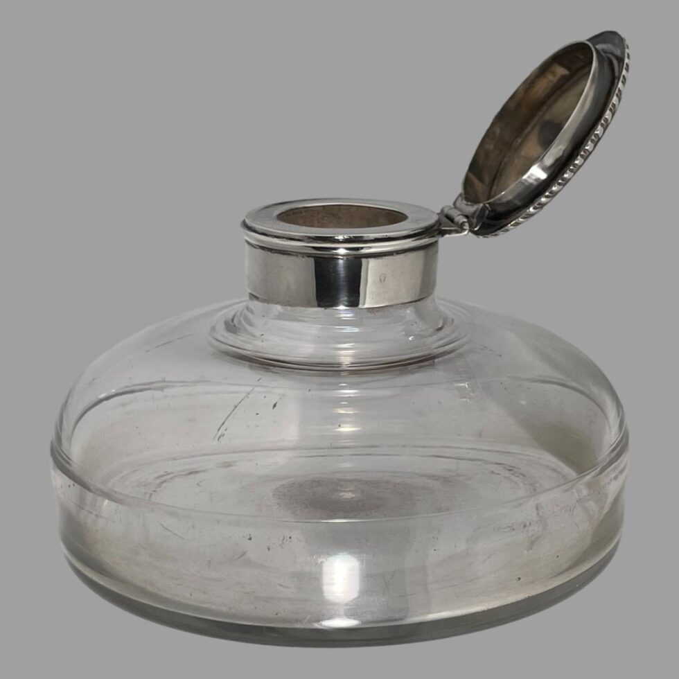 Photo of antique silver mounted inkwell seen from a side angle with the lid open to the right.