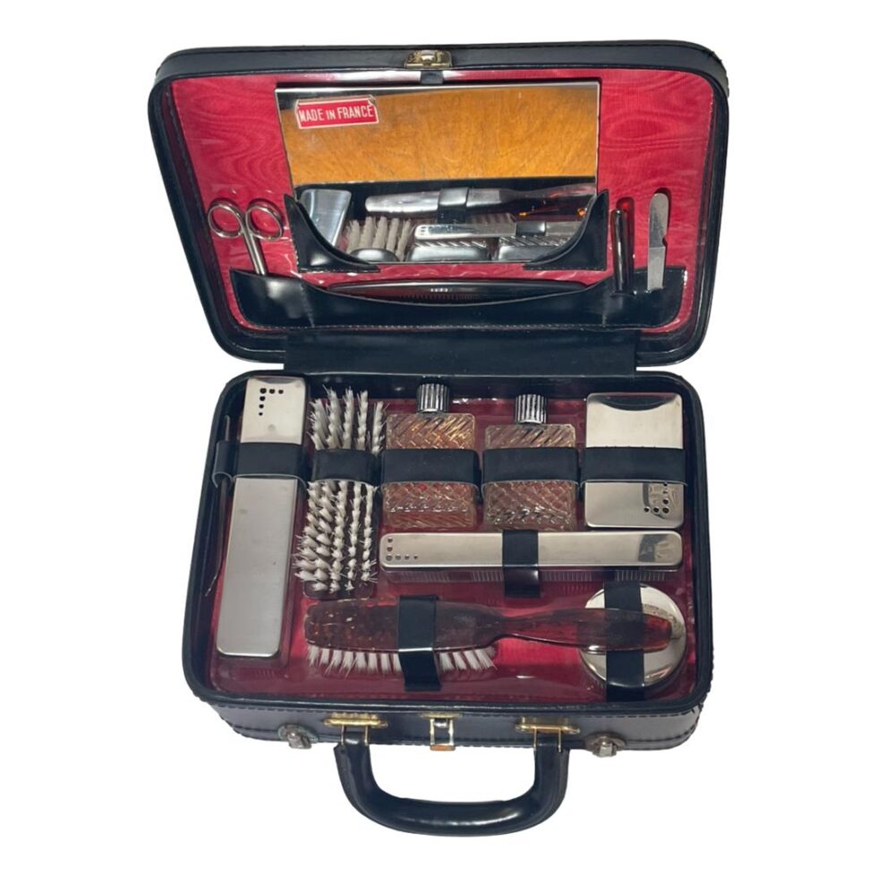 Photo looking down into the contents of the vanity case with all pieces neatly inside their fitted slots. The mirror is also in place inside the lid flanked to the bottom left & right by the nail care implements.