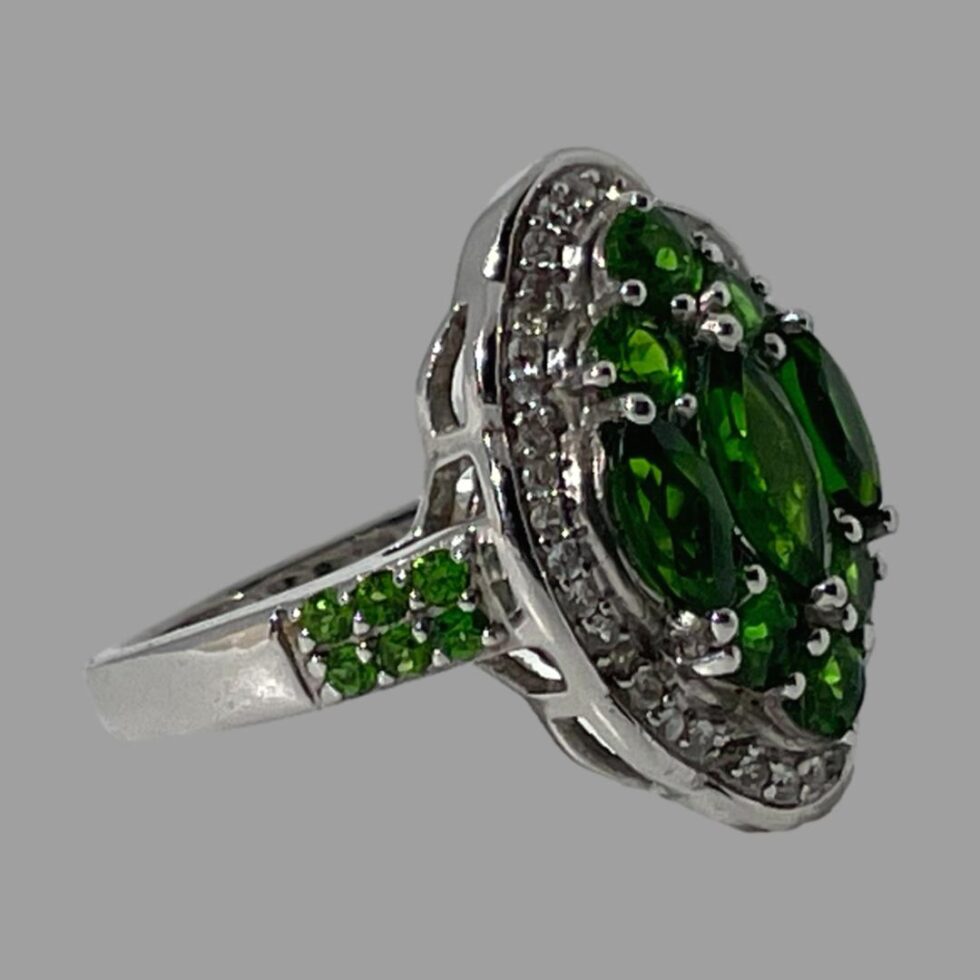 Photo of chrome diopside ring on a flat surface with the ring front facing right. One shoulder with the 3 rows of 2 stones is clearly shown.