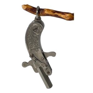 Main photo of Maus cap gun pendant displayed hanging from a twig by its ring bail. Thew gun is in the form of an old flint pistol with scroll work on the handle