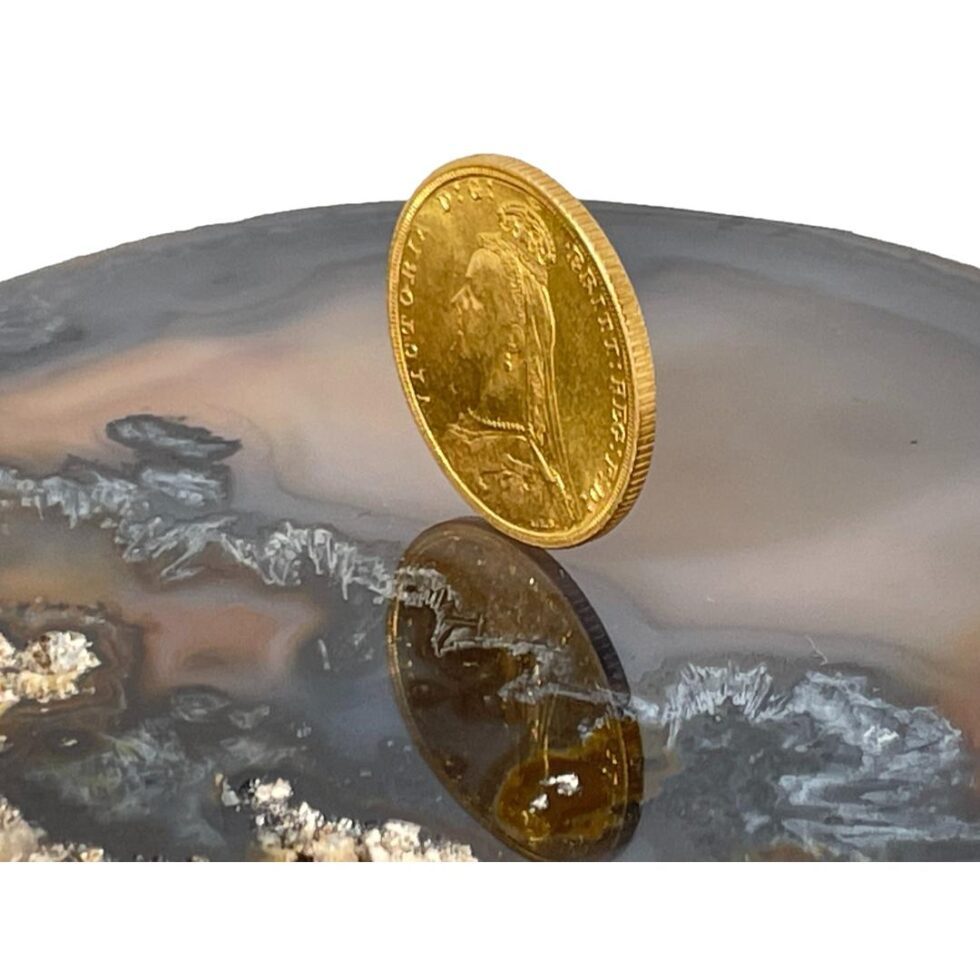 Photo of 22 karat gold sovereign still displayed on top of a slice of natural agate with the coin now angled to show the depth. The obverse side is facing towards the bottom left corner.