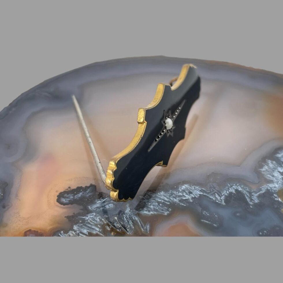 Photo of mourning brooch still on top of the agate slice this time looking at it from a slight side angle looking diagonally and downward. The brooch pin is open and is holding the brooch upright.