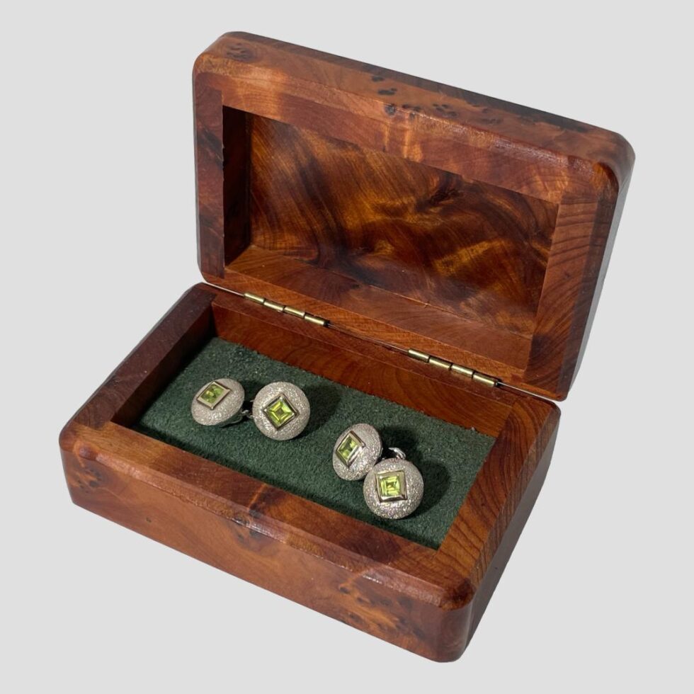 Main photo of Links silver peridot cufflinks displayed inside their wooden box with all the main sides of the cufflinks on display (all sides with peridot) The box appears to be a walnut burr and is a rich orangey brown and there is some green felt like material inside the box with black elastic where the cufflinks are threaded though.