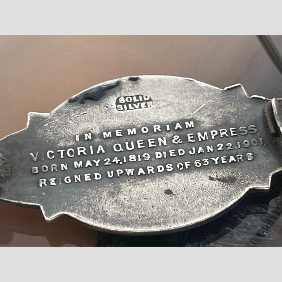 Photo of the back of the brooch with relief wording which reads (at top) Solid Silver and below that In memoriam Victoria Queen & Empress Born May 24, 1819 Died Jan 22, 1901 Reigned upwards of 63 years