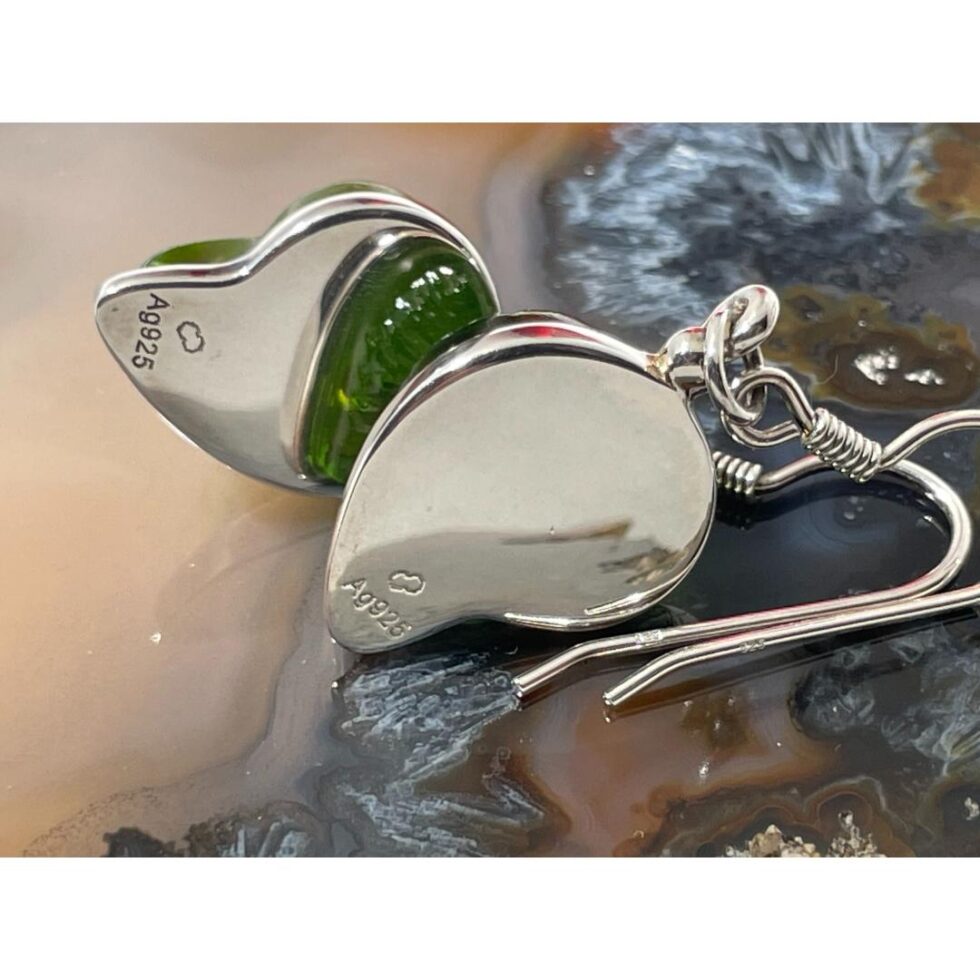 Photo of the earrings still on top of a slice of natural agate and shown on their sides with the back on display. The hallmark to both earrings are on display at the lower point of the silver.