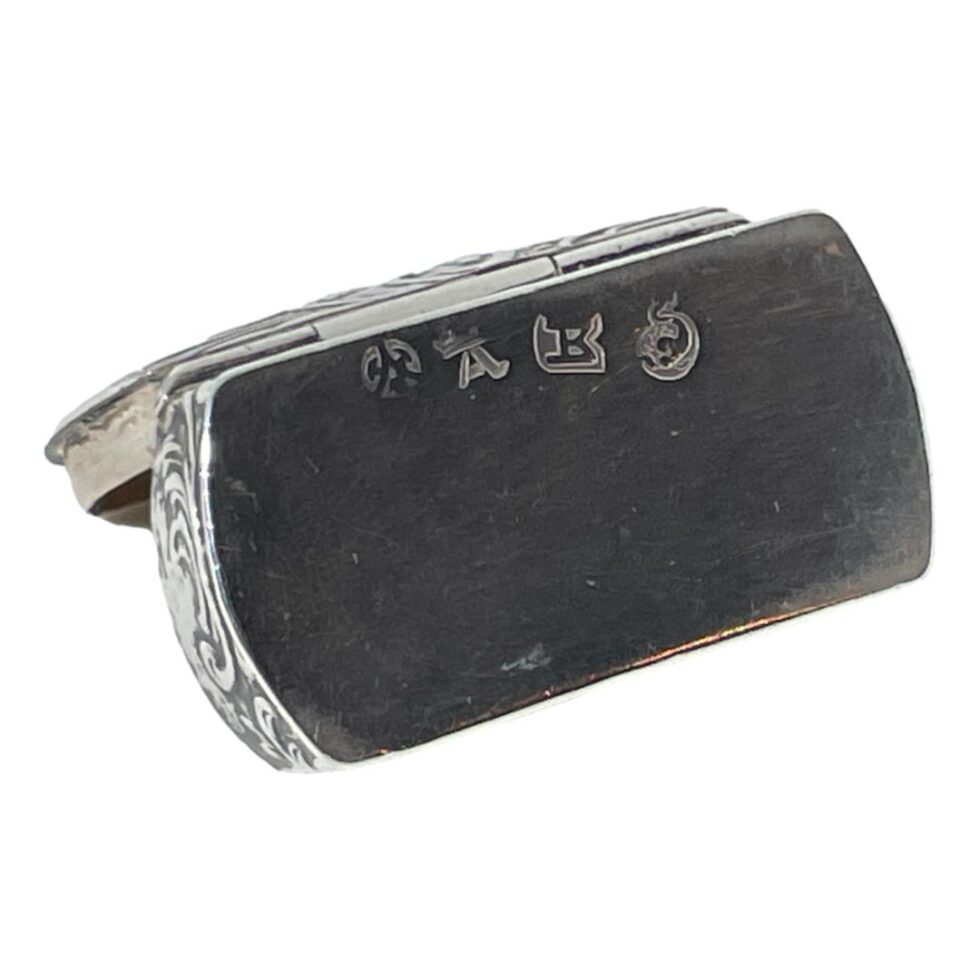 Photo of the small silver box shown open and open side down to reveal the hallmark on the base. There are 4 marks of which one is clearly a dolphin like fish.
