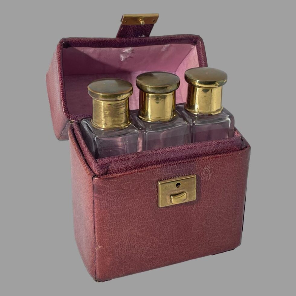 Photo of all 3 perfume bottles displayed inside their open case in row with their brass lids in place. The wear of the silk lining inside the lid is just visible.