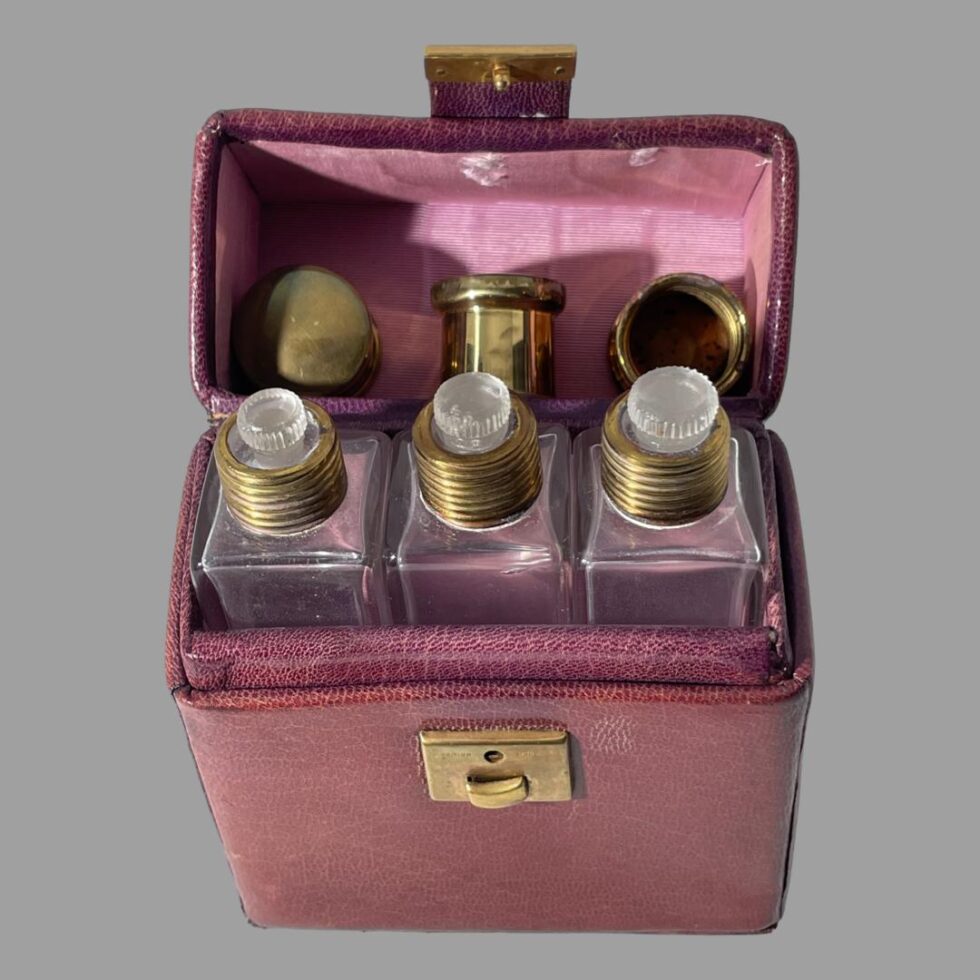 Photo of all 3 bottles inside the case with lids removed and displayed behind them The left bottle has the smalled glass stopper and the brass lid behind is showing the top. The middle bottle has the mid sized glass stopper and is showing the brass lid behind in an upright position. Finally, the 3rd bottle with the largest glass stopper has its brass lid displaying the inside which is corked. Maybe it was made for the 3 bears!