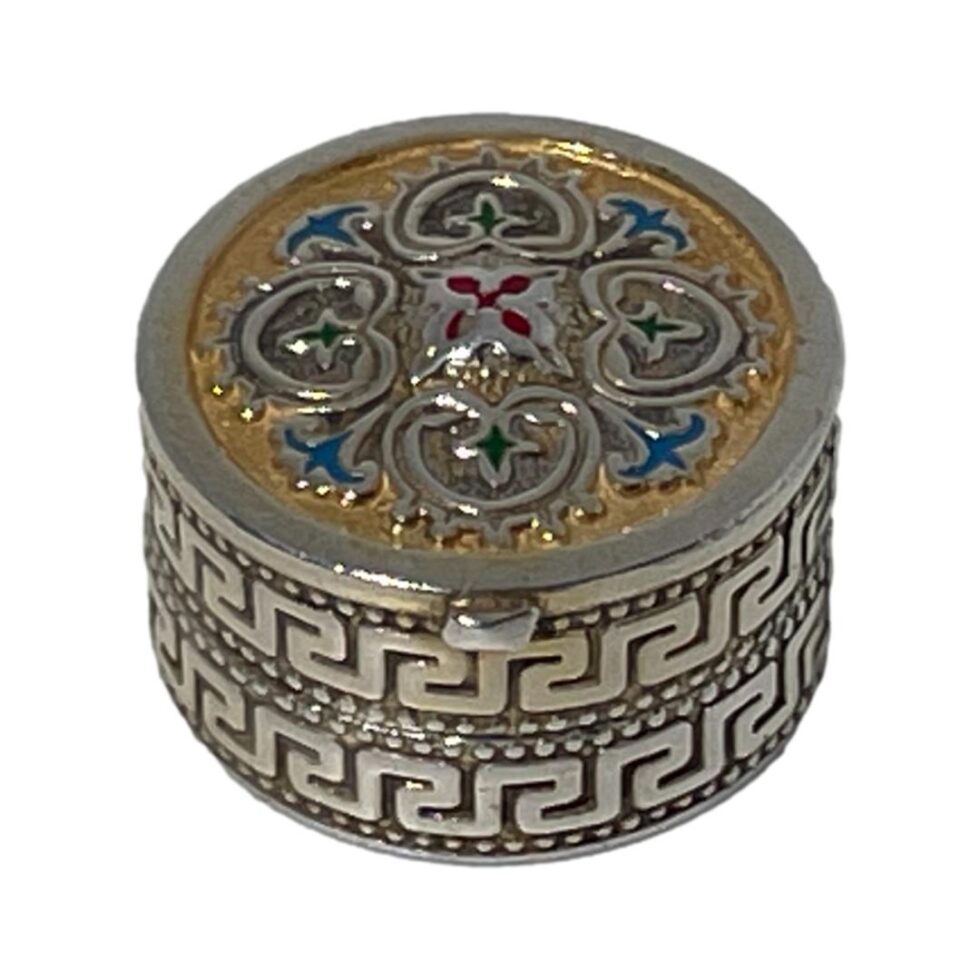Main photo of silver enamel pill box seen from a raised angle looking diagonally down with the enamelled lid in full view and most of the meander pattern around the side.