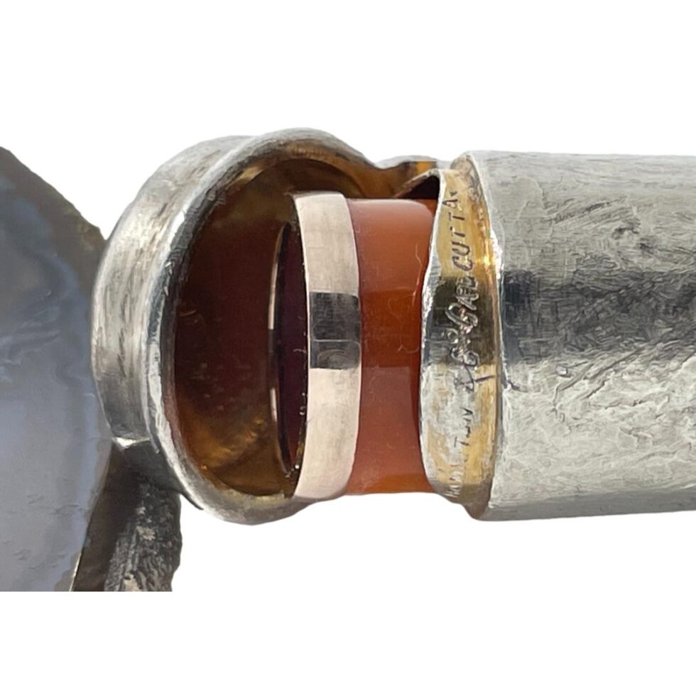 Photo of the cheroot case shown open but not fully with the cheroot sticking out slightly to reveal some of the amber. Part of the impressed 'Hamilton & Co, Calcutta' can be seen around the lip of the inside rim of case.
