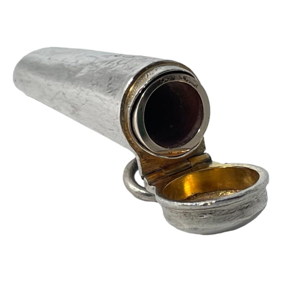 Photo of cheroot case displayed open with the open end facing towards the bottom right corner. The cheroot is inside the case and only the silver rim of it is visible. The gilt inside the lid is visible.