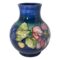 Main photo of large Moorcroft clematis vase seen from an eye level with part of a blue clematis flower on the left, pink clematis to the right and light green foliage and a yellow bud in between. The base colour of the vase is a rich blue, slightly lighter shade than the usual Moorcroft blue but beautiful all the same. Lovely bulbous shape with the floral decoration focused around the bulge!
