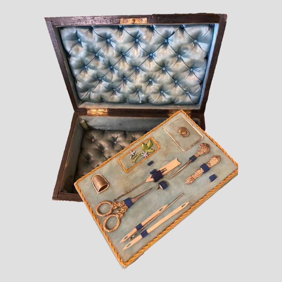 Photo looking down into the Palais Royal sewing box which has its lid open. The contents tray has been lifted and moved across the box to reveal the pale blue padded interior beneath which matches the lid. Useful for storing cotton and buttons etc