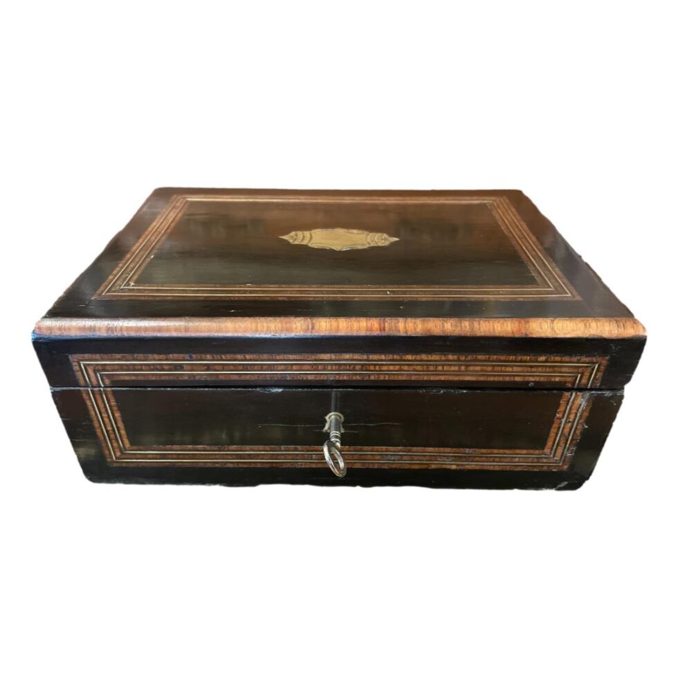 Photo of the Palais Royal sewing box shown closed and from the front. The brass cartouche is visible at centre top and the key is in the lock.