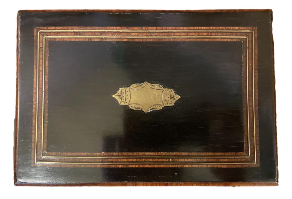 Photo of the top of box lid showing the empty brass cartouche and the wood & brass inlay around the bow edge.