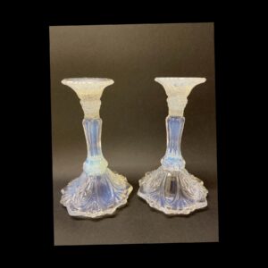 Main photo of 1930s Vaseline glass candlesticks displayed side by side at an eye level. The sconce area appears white but has flecks of white and blue and below the sconce the candlesticks are an almost luminescent Vaseline blue. The background is a dark grey to show up the colours of the candlesticks better.