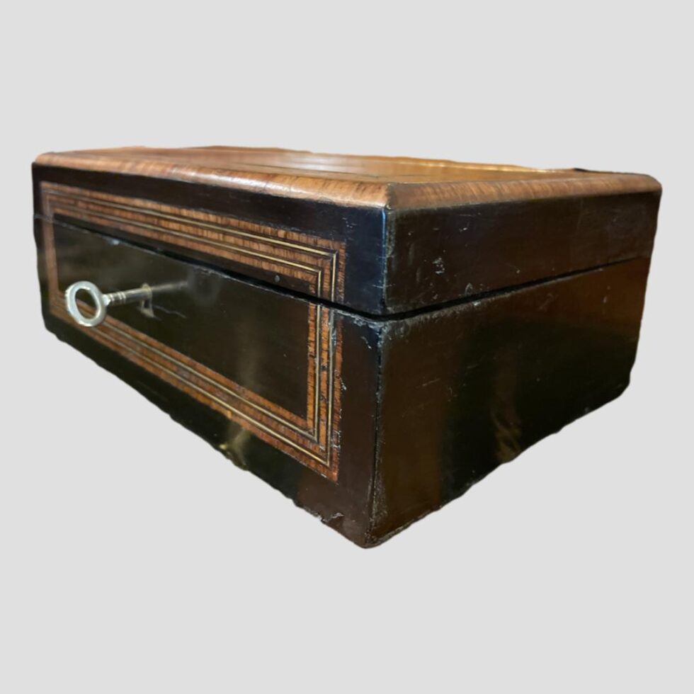 Photo of the sewing box shown closed and from a diagonal eye level so one corner is in the centre foreground. The key is in its lock.